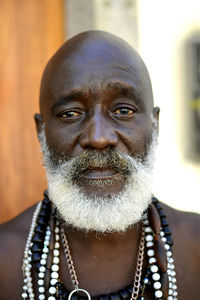 Close-up portrait of bearded bald senior man wearing various necklaces outdoors