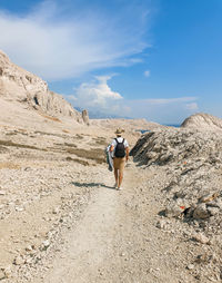 Rear view of young man walking on gravel path through arid terrain in summer.