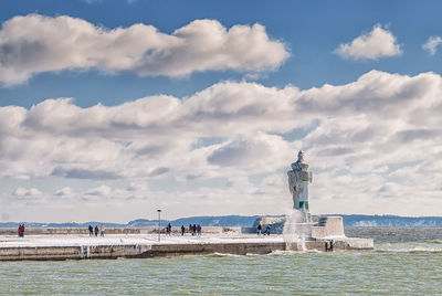 Lighthouse in sea against cloudy sky