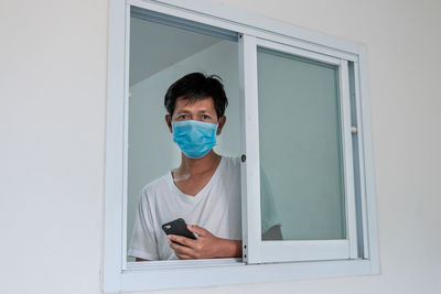 Portrait of mature man wearing flu mask seen through window