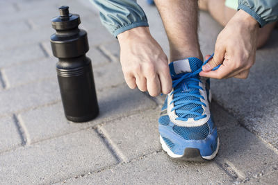Low section of man tying sport shoelace by water bottle on street