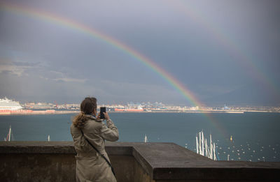 Person in the rain photographing a rainbow over the city of naples