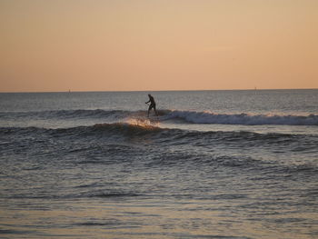 Silhouette man standing in sea against clear sky during sunset