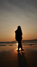 Silhouette woman standing on beach against sky during sunset