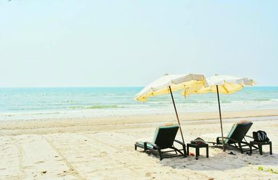 Deck chairs with parasols at beach against clear sky