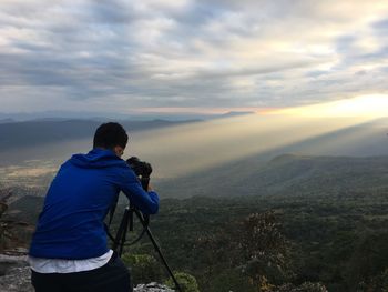 Rear view of man photographing on landscape against sunset sky