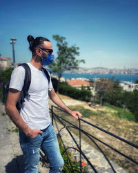 Man wearing sunglasses standing by railing against blue sky