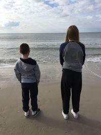 Rear view of brother and sister standing on shore at beach