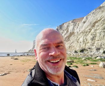 Portrait of cheerful man at beach against clear sky