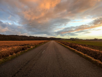 Road amidst field against sky during sunset