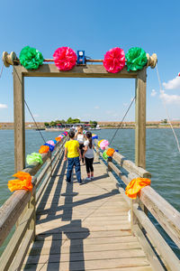 People on pier by sea against sky