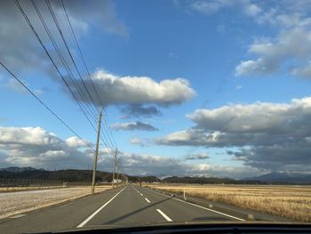 Road by electricity pylon against sky