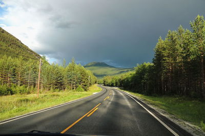 Country road by trees against sky