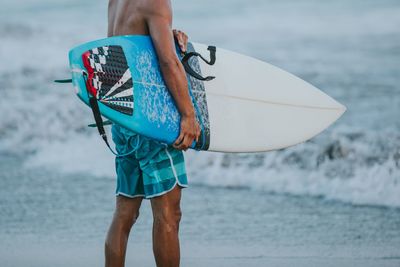 Midsection of man with surfboard standing on beach