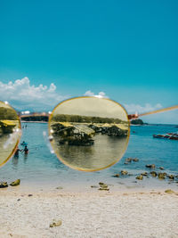 Scenic view of sea seen through sunglasses against blue sky