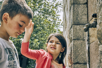 Close-up of siblings standing by faucet on wall