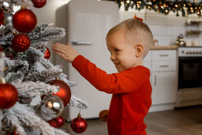 Portrait of happy boy looking at decorative toy ball by christmas tree