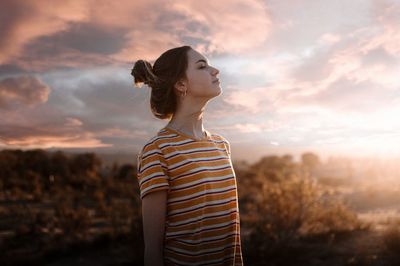 Woman with eyes closed standing against sky during sunset