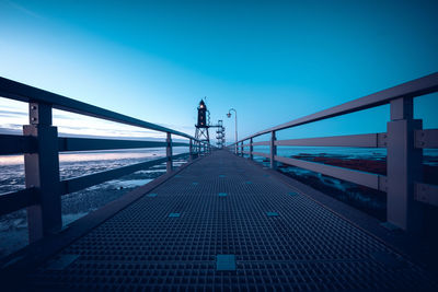 Rear view of people walking on footbridge against clear blue sky