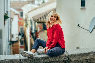 Side view of young woman sitting on railing in city