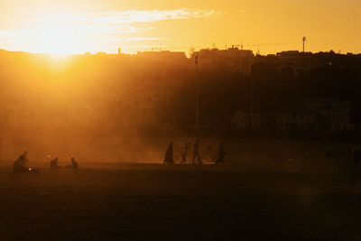 Silhouette people on land against sky during sunset