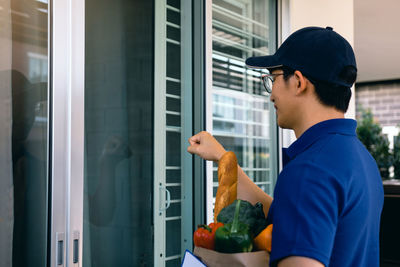 Man holding glass while standing by window