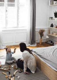 High angle view of baby boy holding toy teacup while sitting with mother on rug in bedroom