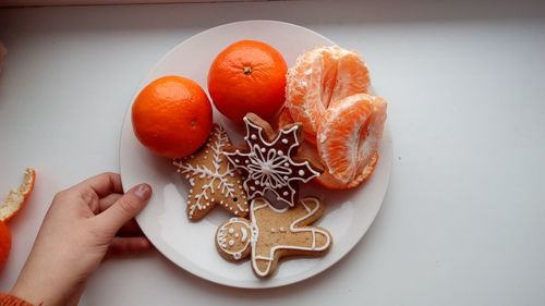 High angle view of hand holding gingerbread cookies and orange fruits in plate