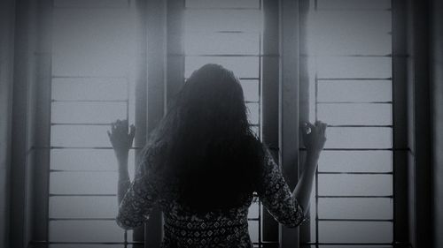 Rear view of woman standing by window at home