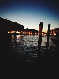 Silhouette of wooden posts in river against sky