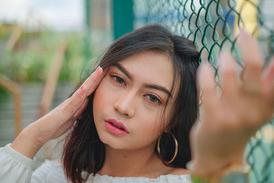 Close-up portrait of young woman standing against chainlink fence