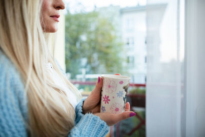 A close-up view of a blonde woman who is looking outside through a window.