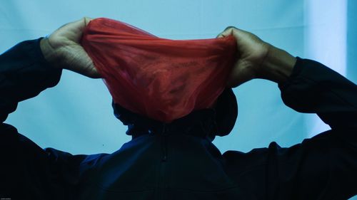 Low angle view of man holding red textile in front of face while standing