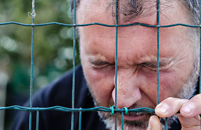 Close-up portrait of man holding chainlink fence