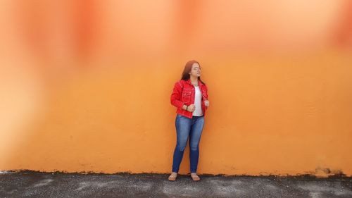 Portrait of young woman standing against orange wall