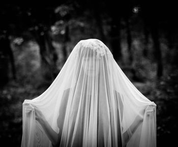 Woman covered with fabric standing against trees