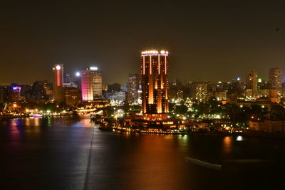 Illuminated buildings by river against sky in city at night