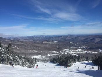 People skiing on snowcapped mountain against cloudy sky