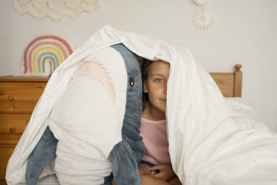 Girl hiding under blanket with shark toy in children's room