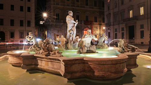 Statue by fountain in city at night