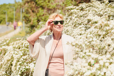 Elderly woman posing among bushes with white flowers