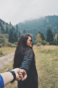 Cropped hand of man holding woman on field against mountain