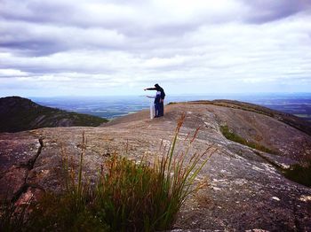 Rear view of man standing on mountain against cloudy sky