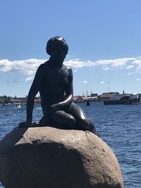 Statue of man sitting by sea against sky