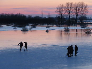 Silhouette people on lake against sky during sunset