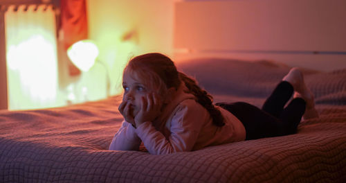 Boy looking away while relaxing on bed at home