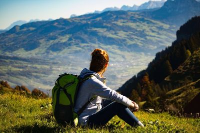 Side view of young woman with backpack sitting on mountain