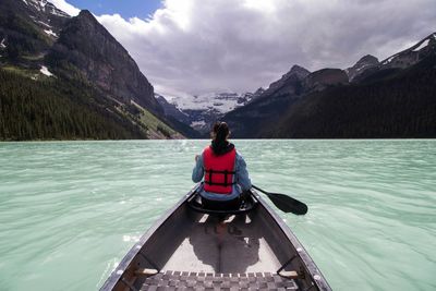 Rear view of woman rowing rowboat in lake towards mountains