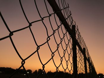 Close-up of chainlink fence against sky during sunset