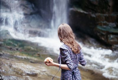 Rear view of girl holding food while looking at waterfall